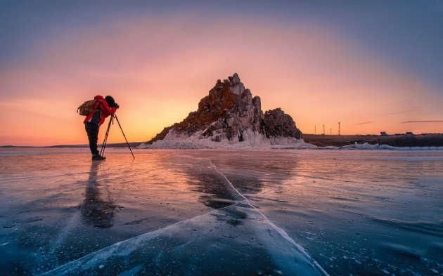 Mann mit Kamera auf Stativ in Eislandschaft vor einem Berg bei Sonnenuntergang