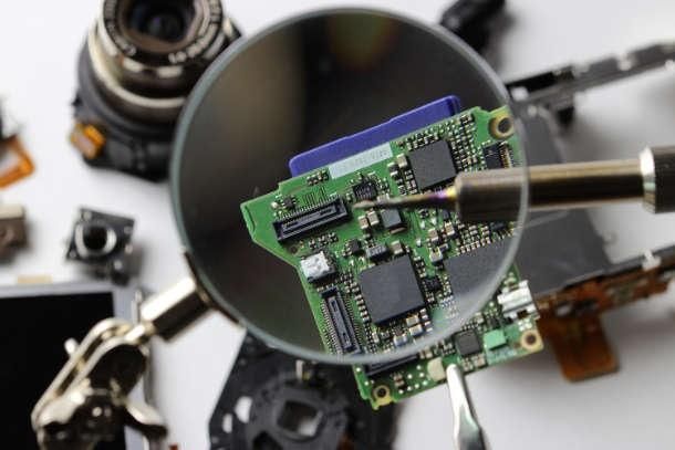 Elektronische Leiterplatte unter der Lupe mit Lötkolbenspitze